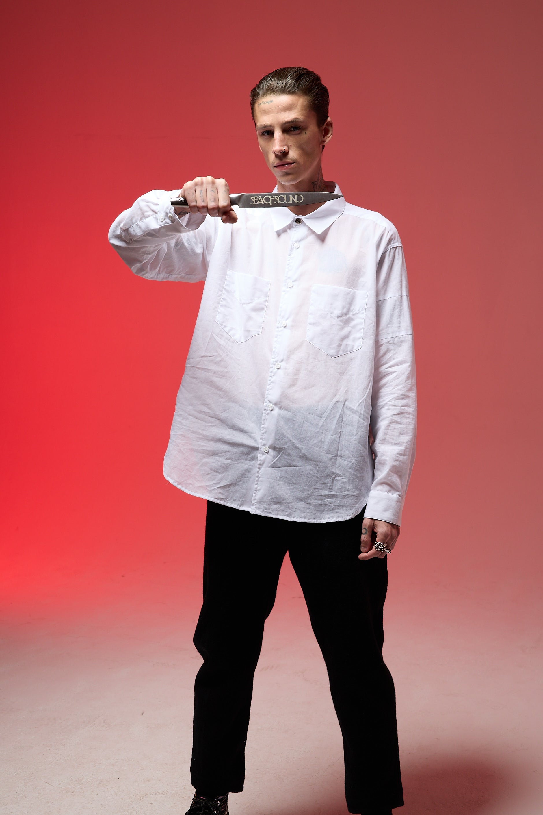 A model is wearing a white button up with black pants while holding the Sea Of Sound Together Carving Knife in their left hand